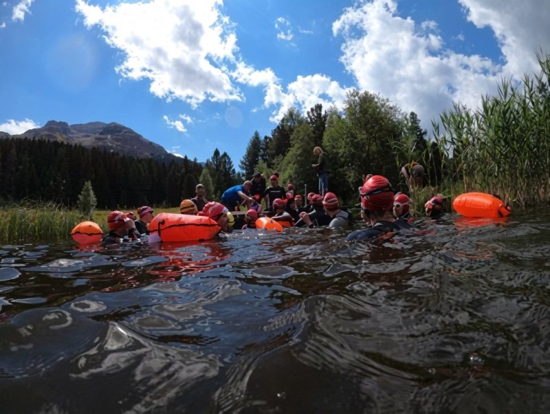Gruppe mit orangen Schwimmbojen in einem Bergsee im Engadin